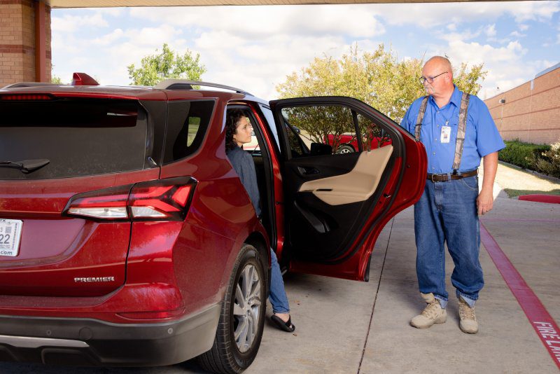 A man holds the door to a car open as a woman prepares to exit